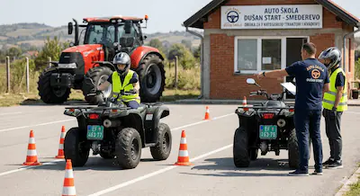 Učenik Auto škole Dušan Start u Smederevu vežba vožnju zelenog kvada na poligonu, dok instruktor pokazuje pravac. U pozadini se vidi crveni traktor i zgrada škole.